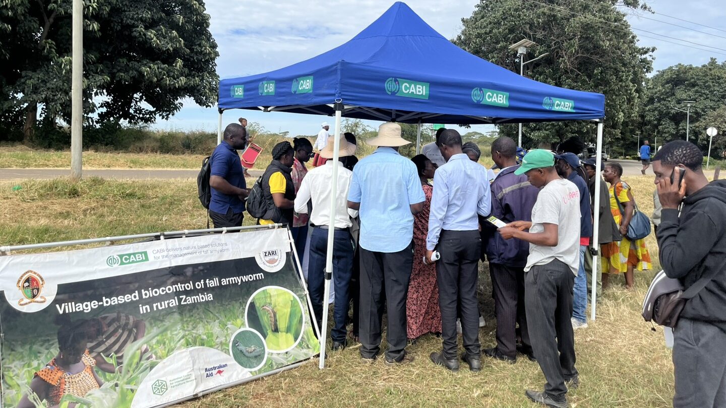A group of people gather around the CABI, UNZA and ZARI stand, whose team are presenting at the ZARI field day.