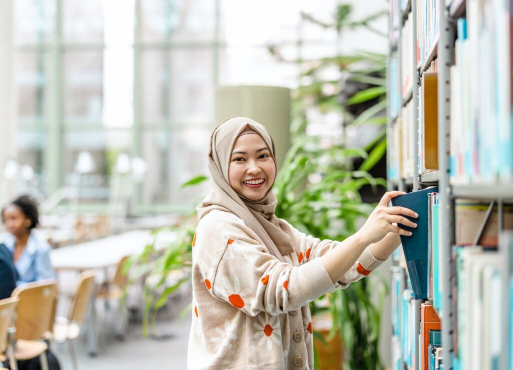 Woman researcher selecting a book from a library bookshelf. Credit: iStock