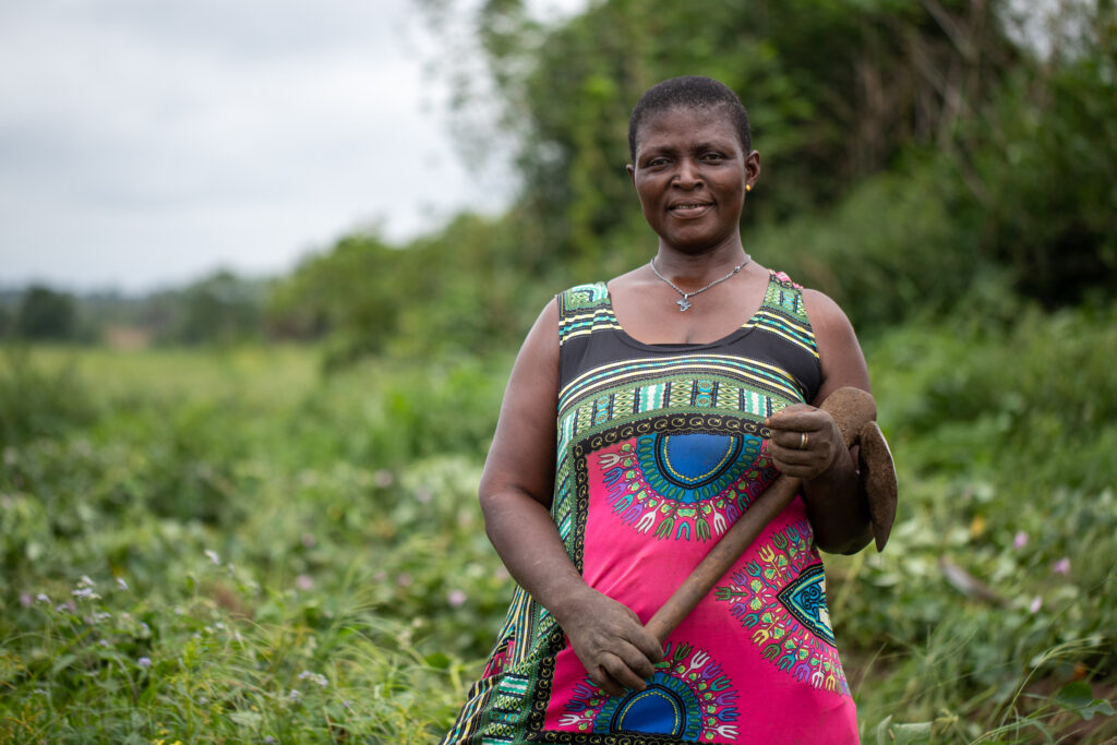 A female farmer in a field in Ghana with an agricultural tool in her hand.