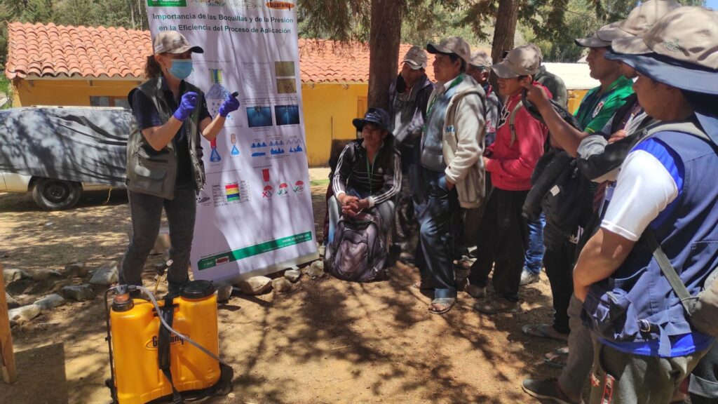 A woman instructor demonstrates the safe usage of pesticides to farmers in an Ecuadorian village 