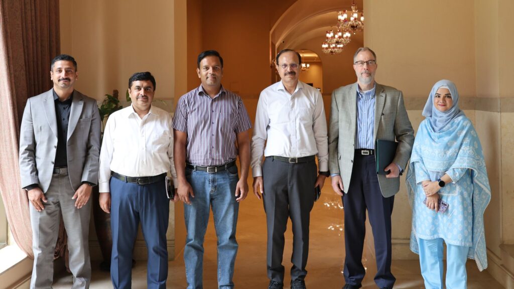 Six project representatives standing together for a group photograph in a hotel or conference venue.